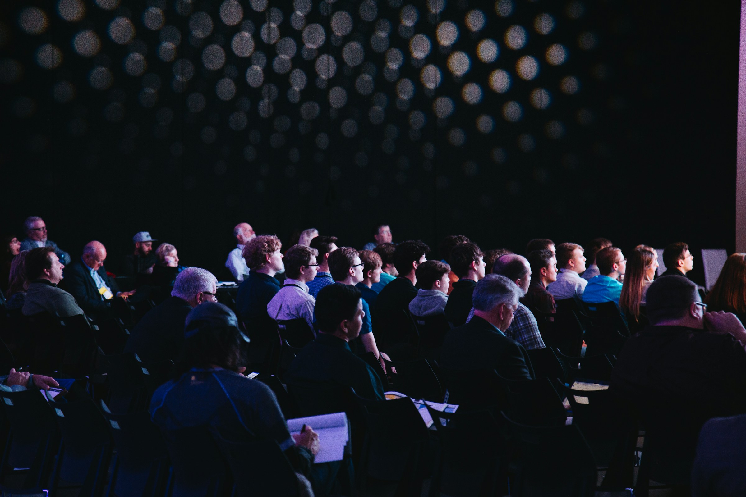A group of people sitting in a conference hall all facing in the same direction.